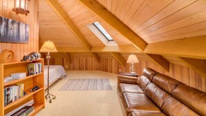 A loft-style bedroom with a sloped ceiling, a skylight, a bed, a leather sofa, a bookshelf, and a floor lamp. - Octagon House Near Leavenworth + Deck (Leavenworth)