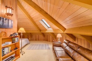 A loft-style bedroom with a sloped ceiling, a skylight, a bed, a leather sofa, a bookshelf, and a floor lamp.