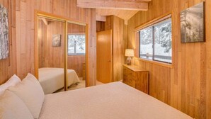 A wooden cabin bedroom with a bed, a bedside table, a mirror, and a window with a snowy view. - Octagon House Near Leavenworth + Deck (Leavenworth)
