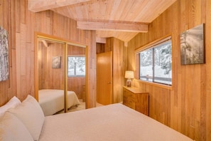 A wooden cabin bedroom with a bed, a bedside table, a mirror, and a window with a snowy view. - The Octagon House - Fun Design in Nature (Leavenworth)