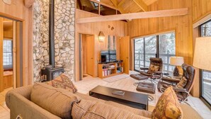 A wooden interior with a stone wall, a fireplace, a television, and a seating area with chairs and a sofa. - Octagon House Near Leavenworth + Deck (Leavenworth)