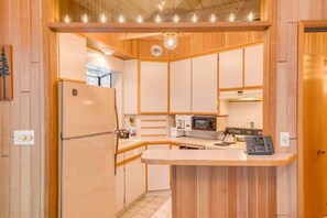 A compact kitchen with a refrigerator, microwave, kettle, and a small island counter.