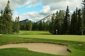 A golf course with a sand bunker, surrounded by dense trees and mountains in the background. - The Octagon House - Fun Design in Nature (Leavenworth)