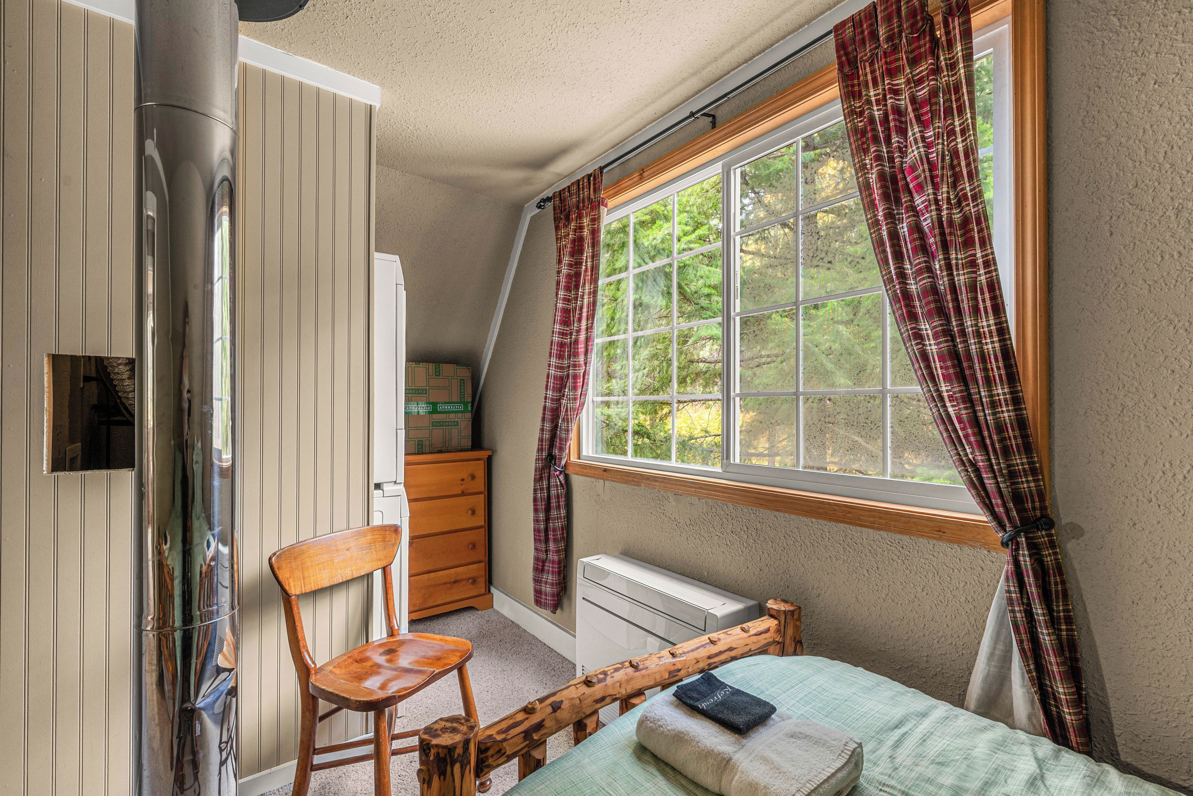 Une chambre à coucher avec un lit, une chaise, un radiateur, une fenêtre avec des rideaux et une tête de lit en bois.
