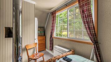 Une chambre à coucher avec un lit, une chaise, un radiateur, une fenêtre avec des rideaux et une tête de lit en bois.