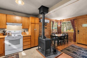 Et køkken med træskabe, en komfur og en brændeovn.