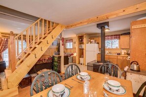 A wooden interior with a dining table set for two, a staircase, and a kitchen area.