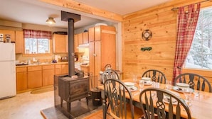 A wooden cabin interior with a dining table, chairs, a kitchen with wooden cabinets, a wood-burning stove, and a window with a view of trees. - Cozy 2BR cabin in Plain/Lake Wenatchee with fireplace, AC, and parking. Pet-friendly (Leavenworth)