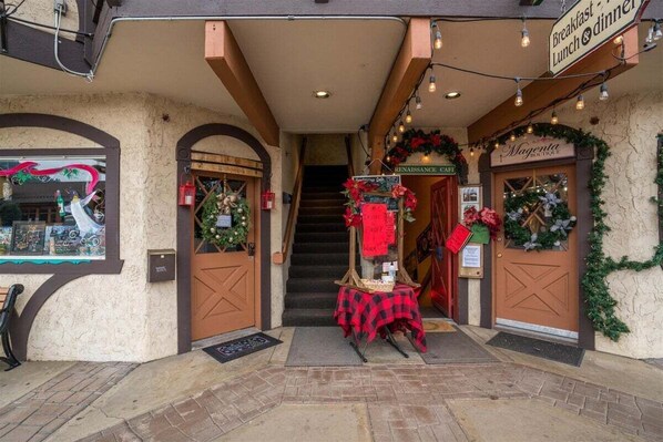 A building entrance with a staircase, a table with a red checkered tablecloth, and signs for a Renaissance Cafe and a boutique.