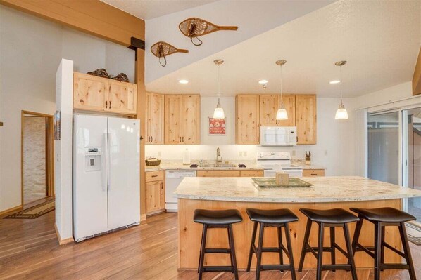Una cocina moderna con armarios de madera, una isla central con taburetes, un refrigerador e iluminación colgante.