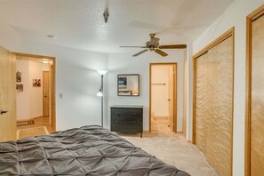Un dormitorio con una cama, ventilador de techo, cómoda y puerta que da a otra habitación.