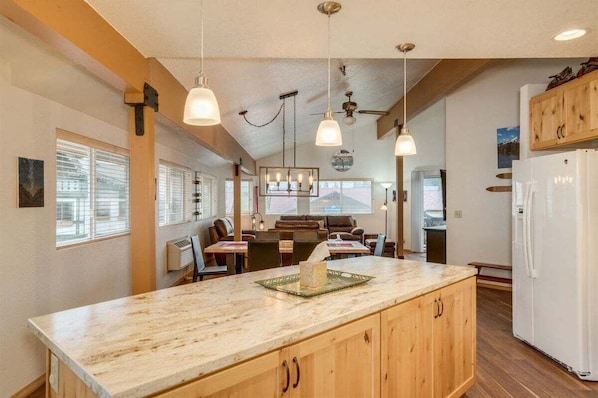 A kitchen with wooden cabinets, a marble countertop, pendant lighting, and a white refrigerator.