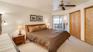 A bedroom with a bed, two bedside lamps, a ceiling fan, and a view of a balcony.