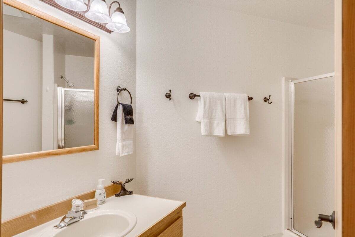 A bathroom with a large mirror, a sink, and a shower.
