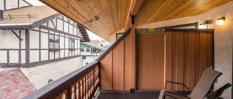 A balcony with wooden railings, a caution sign, and a chair.