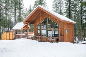 Een houten hut met grote ramen, een veranda en een met sneeuw bedekte dak.