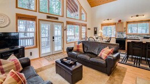 A spacious living room with a large window, a fireplace, and a kitchen area. - 2BR cabin in Leavenworth with hot tub, fireplace, BBQ, 2 kings (Leavenworth)