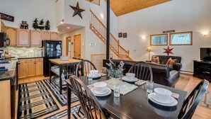 A spacious living area with a dining table set for four, a kitchen with wooden cabinets, a staircase, and a large star decoration on the wall. - 2BR cabin in Leavenworth with hot tub, fireplace, BBQ, 2 kings (Leavenworth)