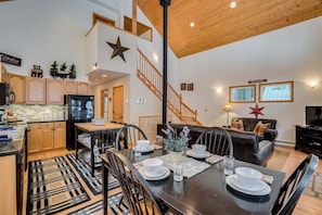 A spacious living area with a dining table set for four, a kitchen with wooden cabinets, a staircase, and a large star decoration on the wall.