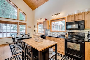 Una cocina con armarios de madera, una estufa negra y una zona de comedor con mesa y sillas.
