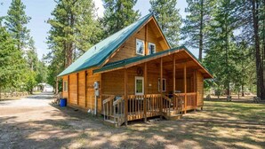 A wooden cabin with a porch, surrounded by trees. - Sunrise Lodge - Fetching Forest Cabin in the Sun! (Leavenworth)