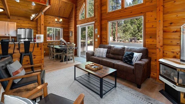 A log cabin interior with a dining area, a sofa, a coffee table, and a fireplace. - Sunrise Lodge - Fetching Forest Cabin in the Sun! (Leavenworth)
