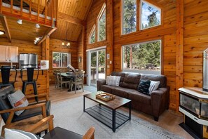 A log cabin interior with a dining area, a sofa, a coffee table, and a fireplace. - Sunrise Lodge - Fetching Forest Cabin in the Sun! (Leavenworth)