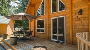 A wooden cabin with a deck, outdoor seating, and a large umbrella. - Sunrise Lodge - Fetching Forest Cabin in the Sun! (Leavenworth)