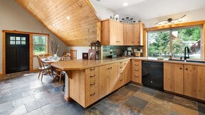 A kitchen with wooden cabinets, a dining table, and a large window. - Leavenworth Views! Peaceful 2BR Lookout Suite (Leavenworth)