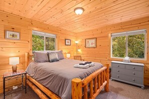 Un dormitorio de cabaña de madera con cama, mesita de noche, lámpara, cómoda y cuadros enmarcados.