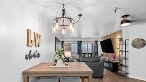 A modern living room with a dining area, a chandelier, and a flat-screen TV.