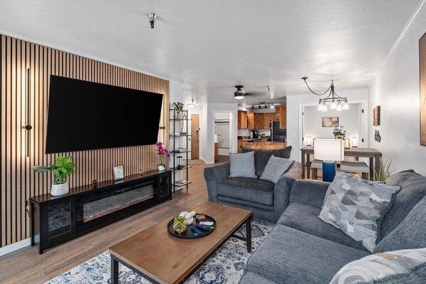 A living room with a flat-screen TV, grey sofas, a wooden coffee table, and a patterned rug.