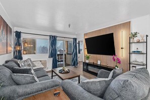 A modern living room with a sofa set, a coffee table, a flat-screen TV, and a wooden accent wall. - Wolfgang Downtown Suites, #34 (Leavenworth)