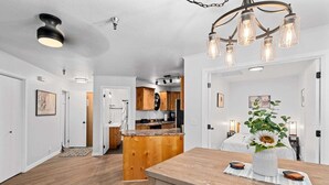 Quarto amplo com uma mesa de jantar de madeira, área de cozinha ao fundo e luminária no teto.