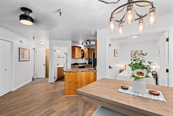 A spacious room with a wooden dining table, a kitchen area in the background, and a ceiling light fixture. - Wolfgang Downtown Suites, #34 (Leavenworth)