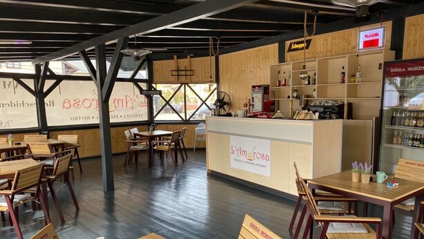 Un restaurant avec des tables et des chaises en bois, un comptoir où est affiché le menu, et une enseigne pour la bière Birra Moretti.