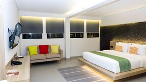 A modern hotel room with a bed, a sofa, a desk, and a TV mounted on the wall. - Qubika Boutique Hotel (Gading Serpong)