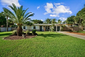A single-story house with a well-maintained lawn, a palm tree, and a wooden fence.