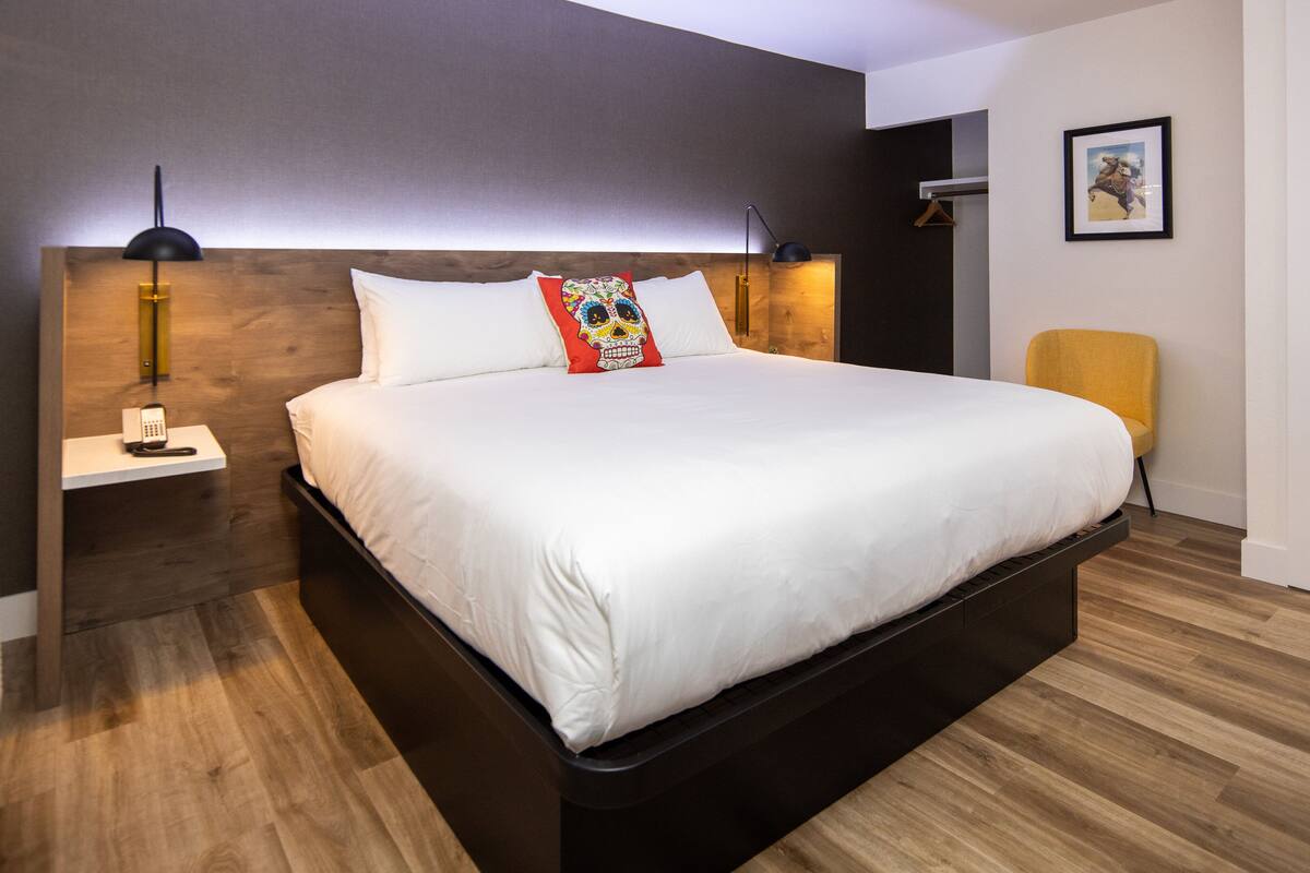 Ein modernes Hotelzimmer mit einem großen Bett, einem Nachttisch mit Telefon, einem Sessel und einer Tür.