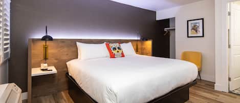 A modern hotel room with a large bed, a bedside table with a phone, a chair, and a door.