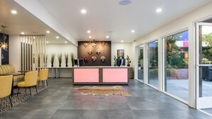 A modern reception area with a central desk, seating area, and a view of the outdoors. - The Catrina Hotel (San Mateo)