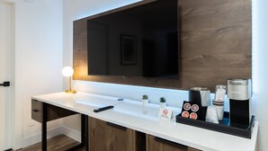 A modern hotel bathroom with a white countertop, a mounted television, a Keurig coffee machine, and a sign prohibiting smoking. - The Catrina Hotel (San Mateo)
