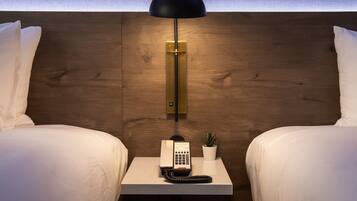 A hotel room with a wooden headboard, two beds, a bedside table with a telephone, a small potted plant, and a black lamp.