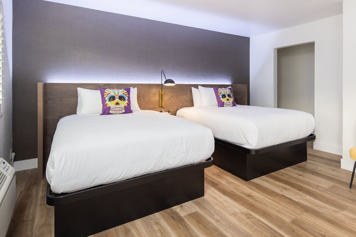 Ein Hotelzimmer mit zwei Betten, Holzboden, einem gelben Stuhl und einem gerahmten Bild an der Wand.