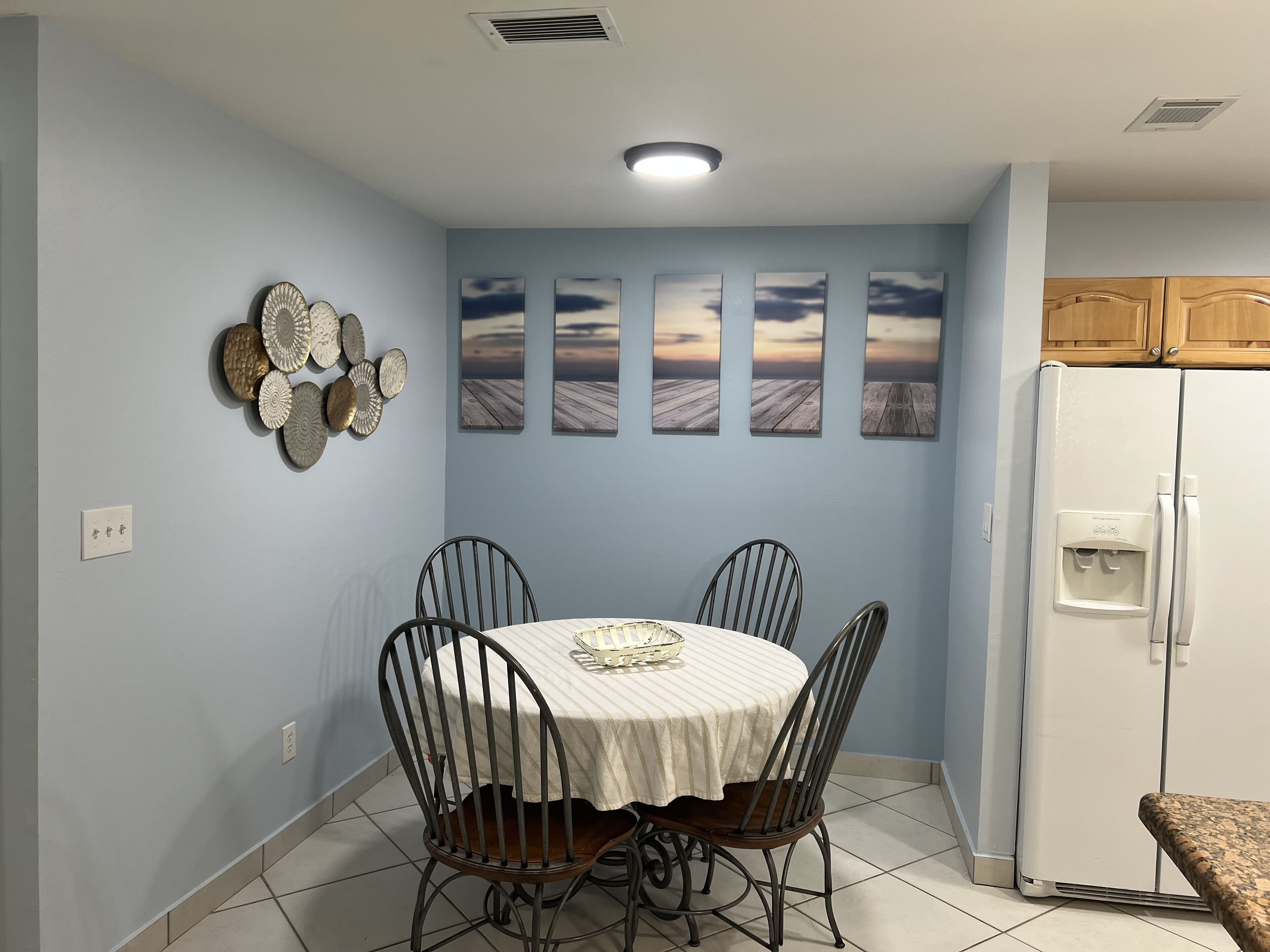 A dining area with a round table, four chairs, and a refrigerator.