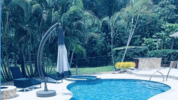 A swimming pool with a curved design, surrounded by lounge chairs and a shaded area. - Lovely Private Cottage, less than 5 miles to the beach!!! (Naples)