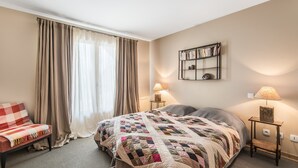 Habitació d'hotel amb un llit gran, dues taules de nit amb làmpades, una biblioteca, una cadira i una finestra amb cortines.