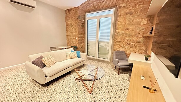 Un salon avec un canapé, une table basse, un mur en pierre et une grande fenêtre.