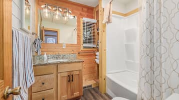 A bathroom with wooden paneling, a sink with a mirror, a shower with a patterned curtain, and a towel hanging on the door.