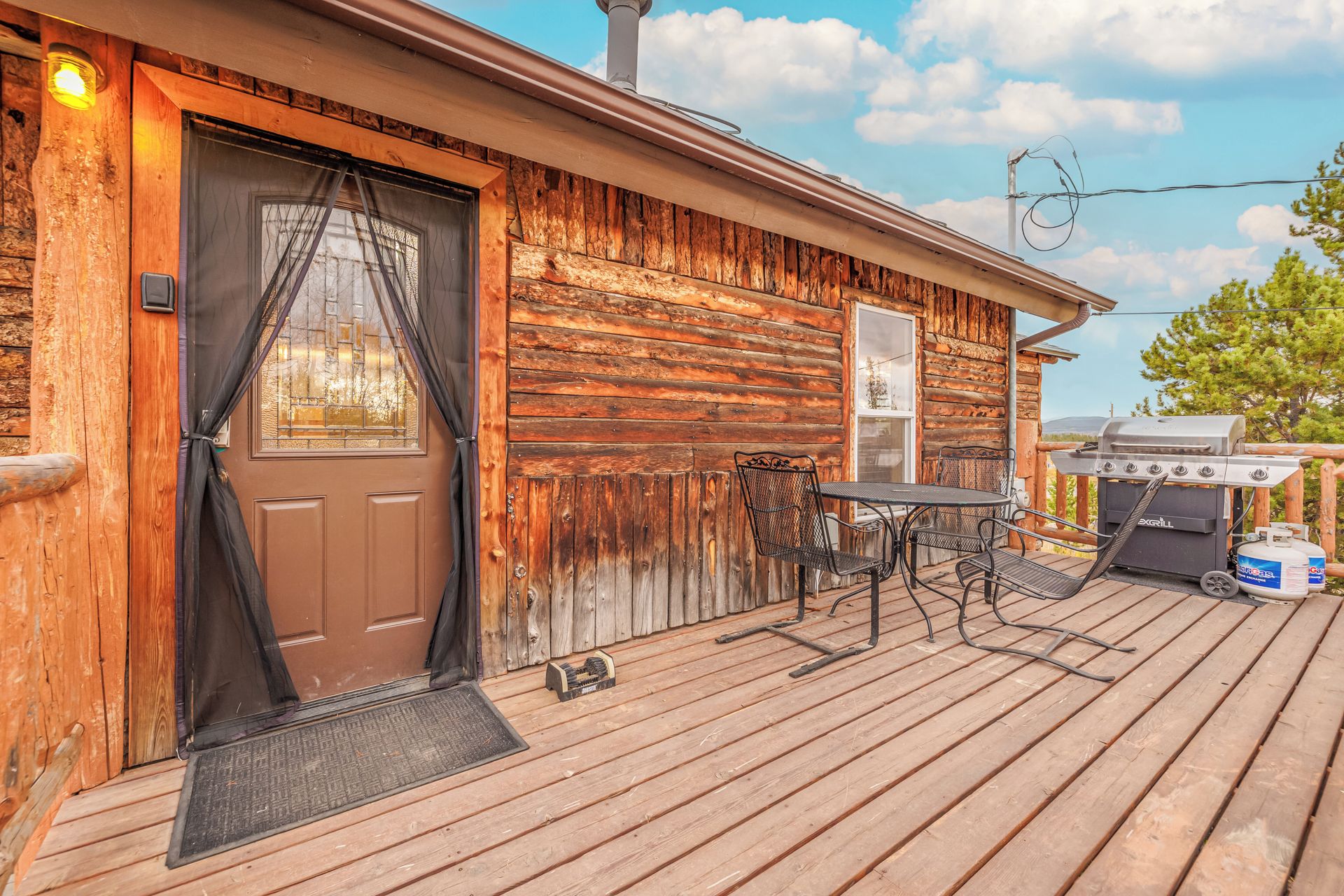 Une cabane en bois avec une porte d’entrée, un petit patio avec une table et des chaises, et un barbecue.